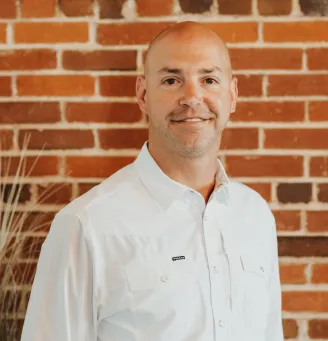 Portrait of Benton Johnson from Big Sky Doors, smiling in front of a red brick wall in the company office.