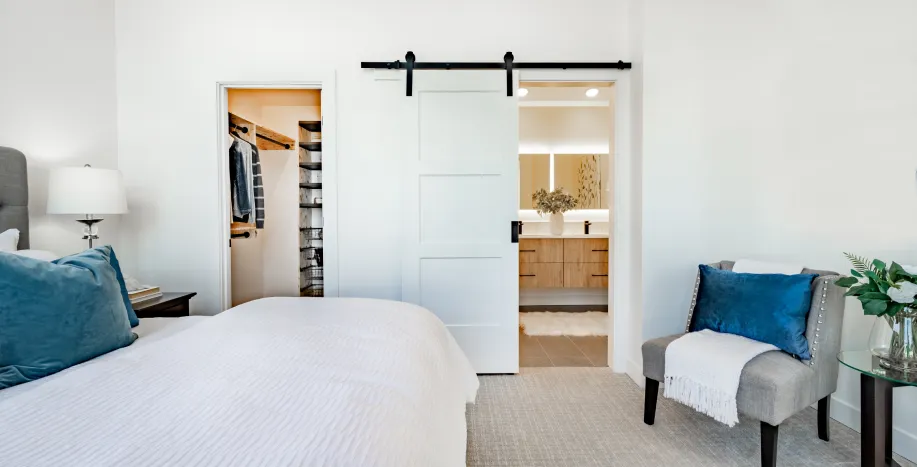 Modern bedroom with a white sliding barn door leading to a bright bathroom, designed by Big Sky Doors.