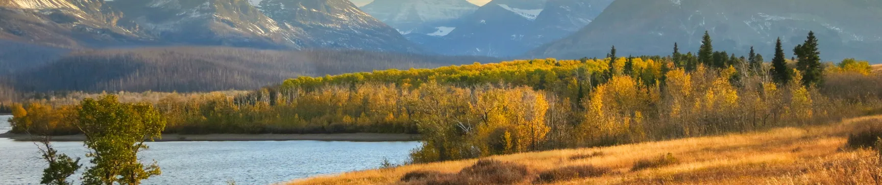 Scenic Montana landscape with autumn trees, lake, and mountain backdrop, representing Big Sky Doors’ Montana roots.
