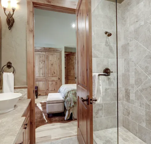 Rustic wood interior door opening from a tiled bathroom to a bedroom, featuring custom craftsmanship by Big Sky Doors.